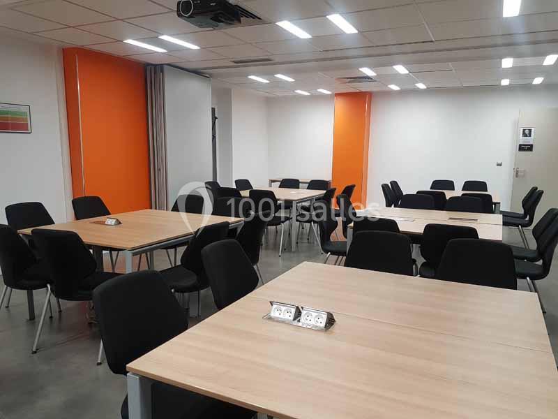 Salle de réunion moderne avec plusieurs tables en bois, chaises noires et murs partiellement orange.
