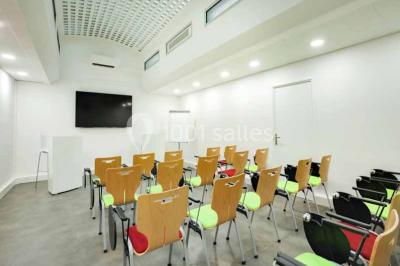 Salle de réunion avec table en bois, chaises noires, mur rouge décoré et écran mural éteint.