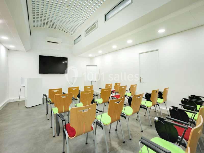 Salle de réunion lumineuse avec des chaises colorées disposées face à un écran mural et un tableau blanc.