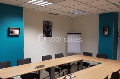 Salle de réunion avec table en bois, chaises noires, mur rouge décoré et écran mural éteint.