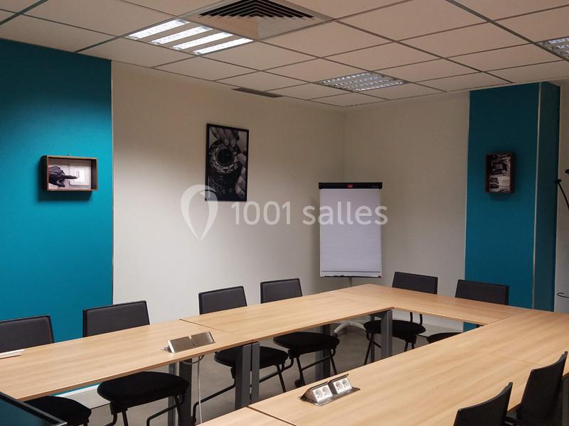 Salle de réunion avec table en bois, chaises noires, murs décorés de cadres et un tableau de conférence.