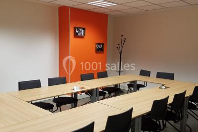 Salle de réunion avec table en bois, chaises noires, mur rouge décoré et écran mural éteint.
