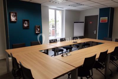Salle de réunion avec table en bois, chaises noires, mur rouge décoré et écran mural éteint.