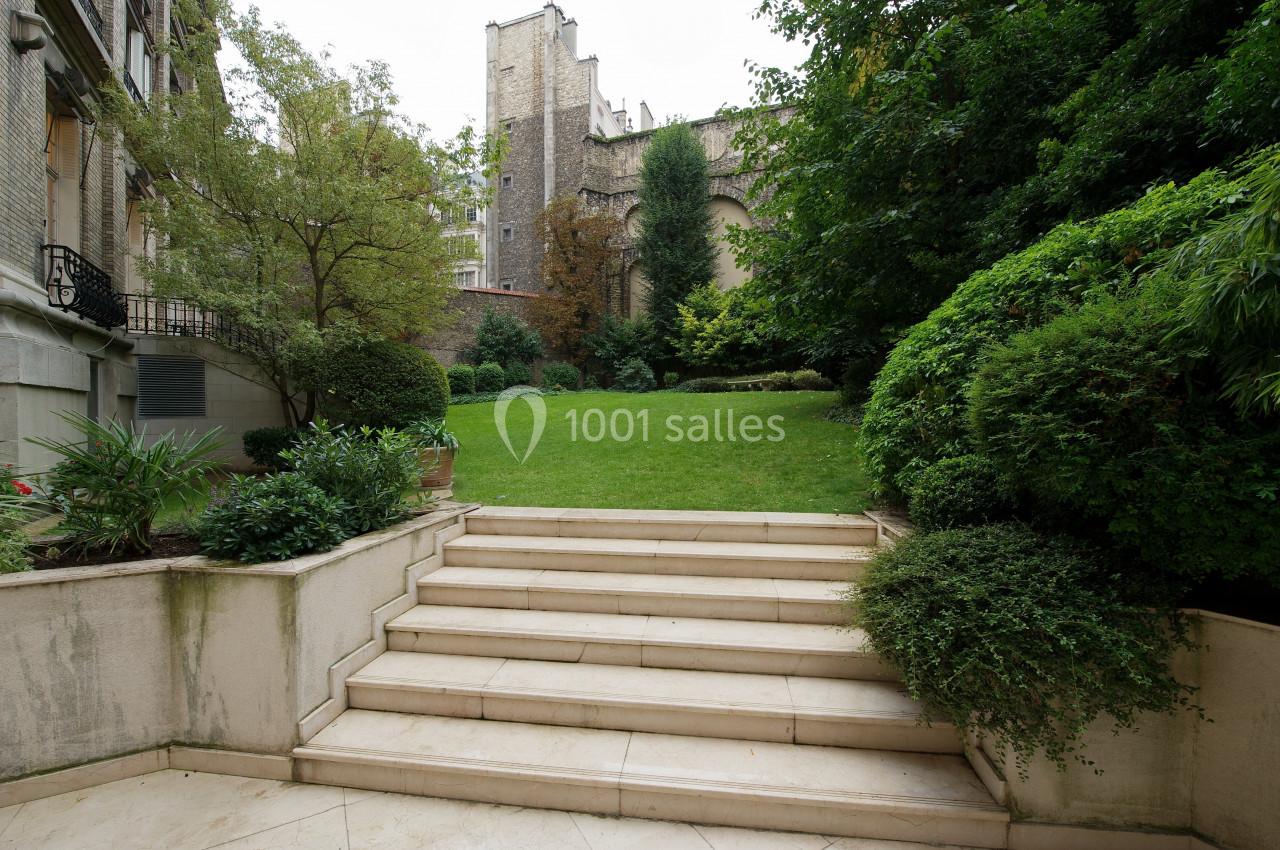 Escalier en pierre menant à un jardin verdoyant entouré de bâtiments en arrière-plan.