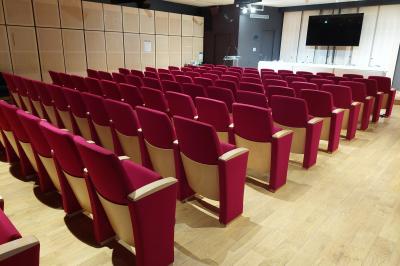 Salle de réunion avec table en bois, chaises noires, mur rouge décoré et écran mural éteint.