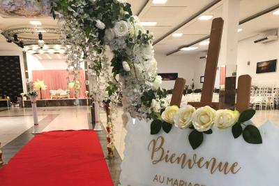 Salle de réception décorée avec des fleurs et éclairages roses, scène équipée de matériel audio en arrière-plan.