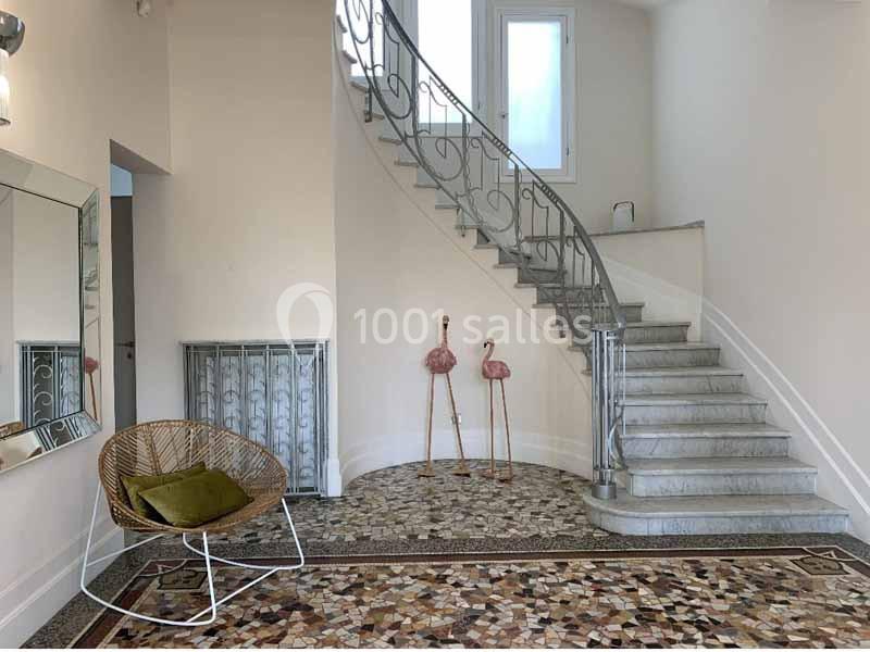 Escalier en colimaçon avec rampe en métal, sol en mosaïque, fauteuil en osier et décorations flamants roses.