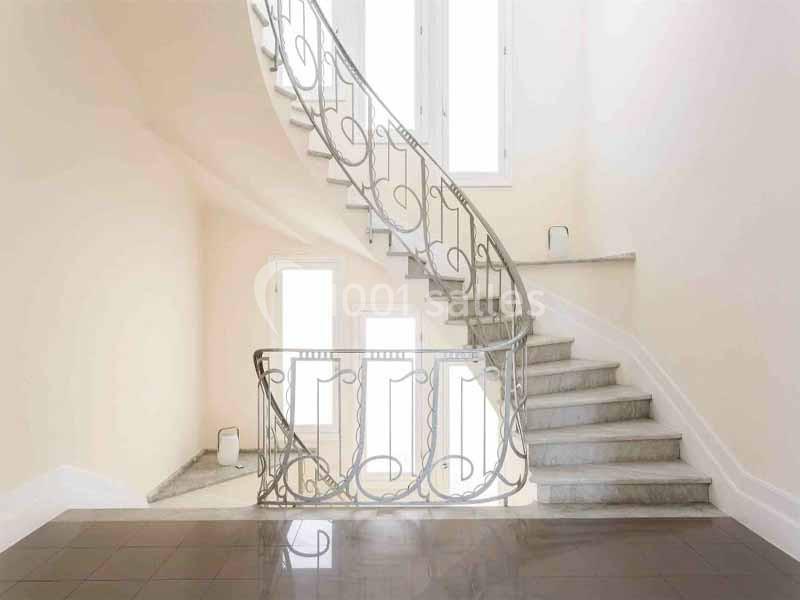 Escalier intérieur en marbre avec rampe en fer forgé, éclairé par des fenêtres laissant entrer une lumière naturelle.