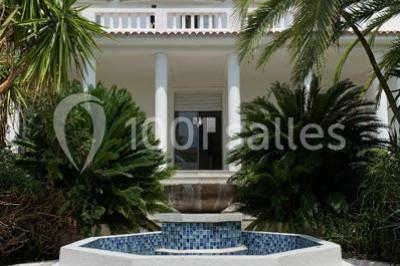 Vue panoramique sur une ville côtière avec des bâtiments, des arbres, la mer et des collines à l'horizon sous un ciel dégagé.