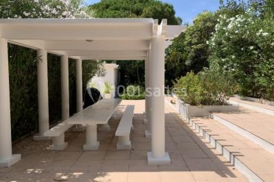 Vue panoramique sur une ville côtière avec des bâtiments, des arbres, la mer et des collines à l'horizon sous un ciel dégagé.