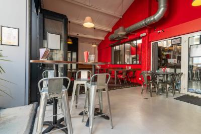 Salle de restaurant moderne avec tables noires, chaises rouges translucides et mur en pierre apparente.