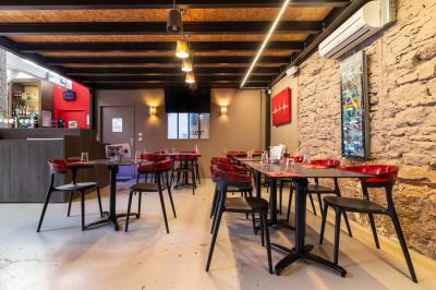 Salle de restaurant moderne avec tables noires, chaises rouges translucides et mur en pierre apparente.