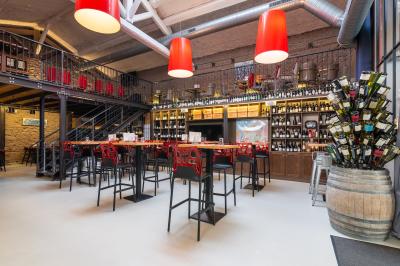 Salle de restaurant moderne avec tables noires, chaises rouges translucides et mur en pierre apparente.
