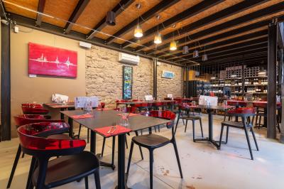 Salle de restaurant moderne avec tables noires, chaises rouges translucides et mur en pierre apparente.