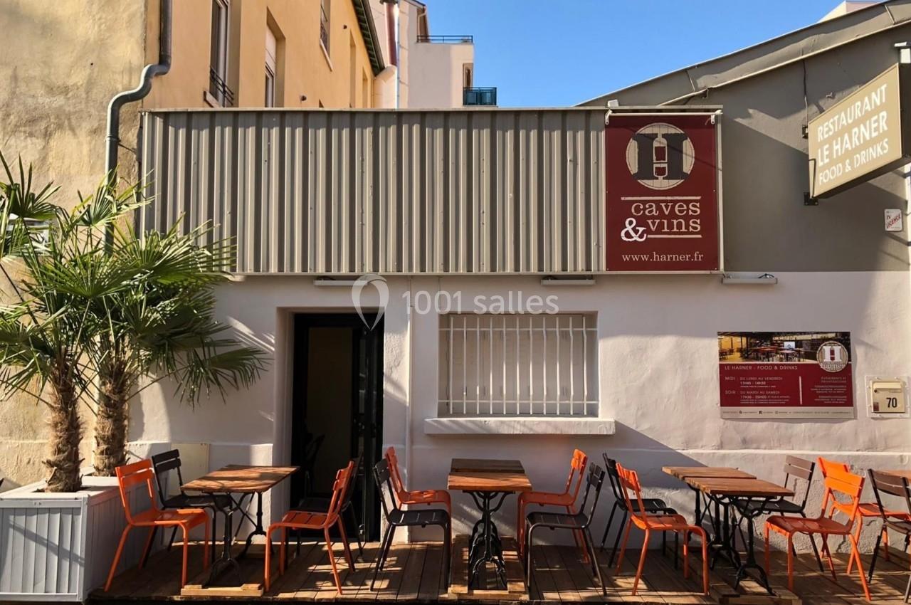 Terrasse extérieure d'un restaurant avec des tables et chaises orange, façade blanche et enseignes visibles.