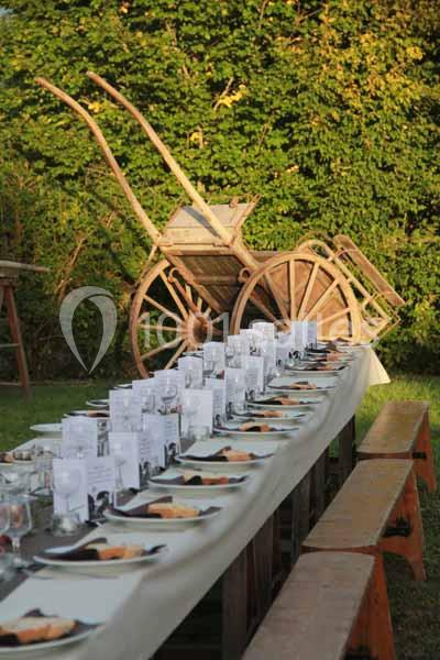 Table dressée en extérieur avec des assiettes et des menus, devant une charrette en bois et un fond de verdure.