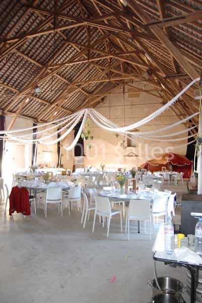 Salle de réception décorée avec des guirlandes blanches suspendues, des tables dressées et des chaises blanches.