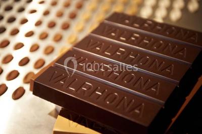 Verres de vin rouge et blanc sur un tonneau en bois, accompagnés de chocolats assortis disposés sur des tablettes.