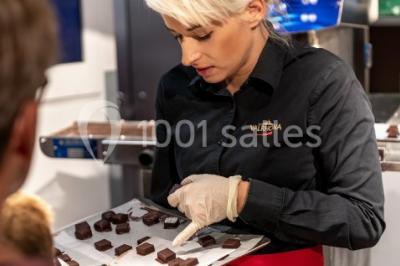 Verres de vin rouge et blanc sur un tonneau en bois, accompagnés de chocolats assortis disposés sur des tablettes.
