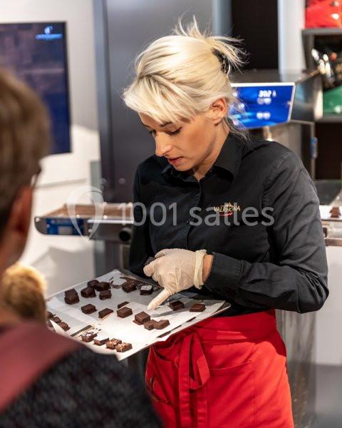 Une femme en tablier rouge présente des chocolats sur un plateau lors d'une démonstration culinaire.