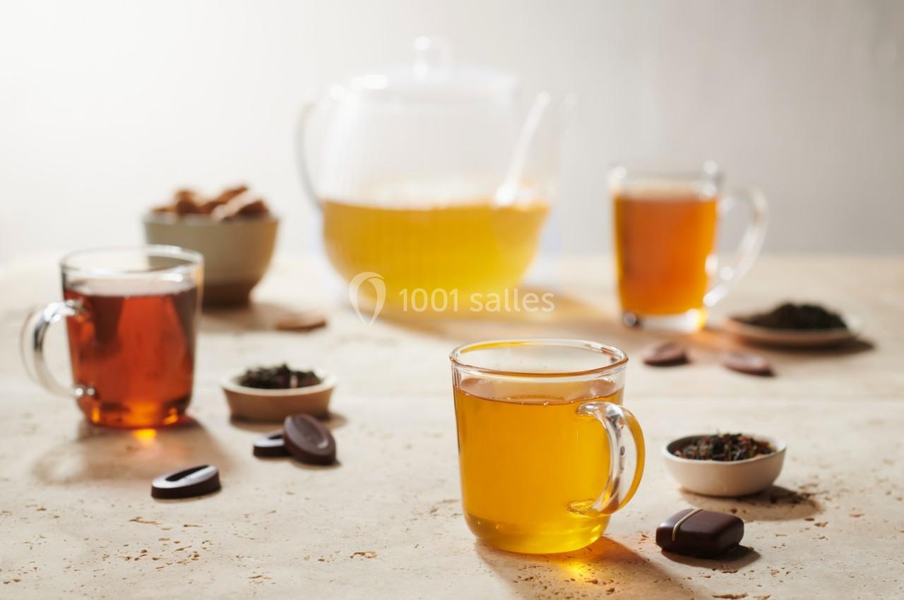 Tasses de thé chaud sur une table avec une théière, des feuilles de thé et des morceaux de chocolat en arrière-plan.