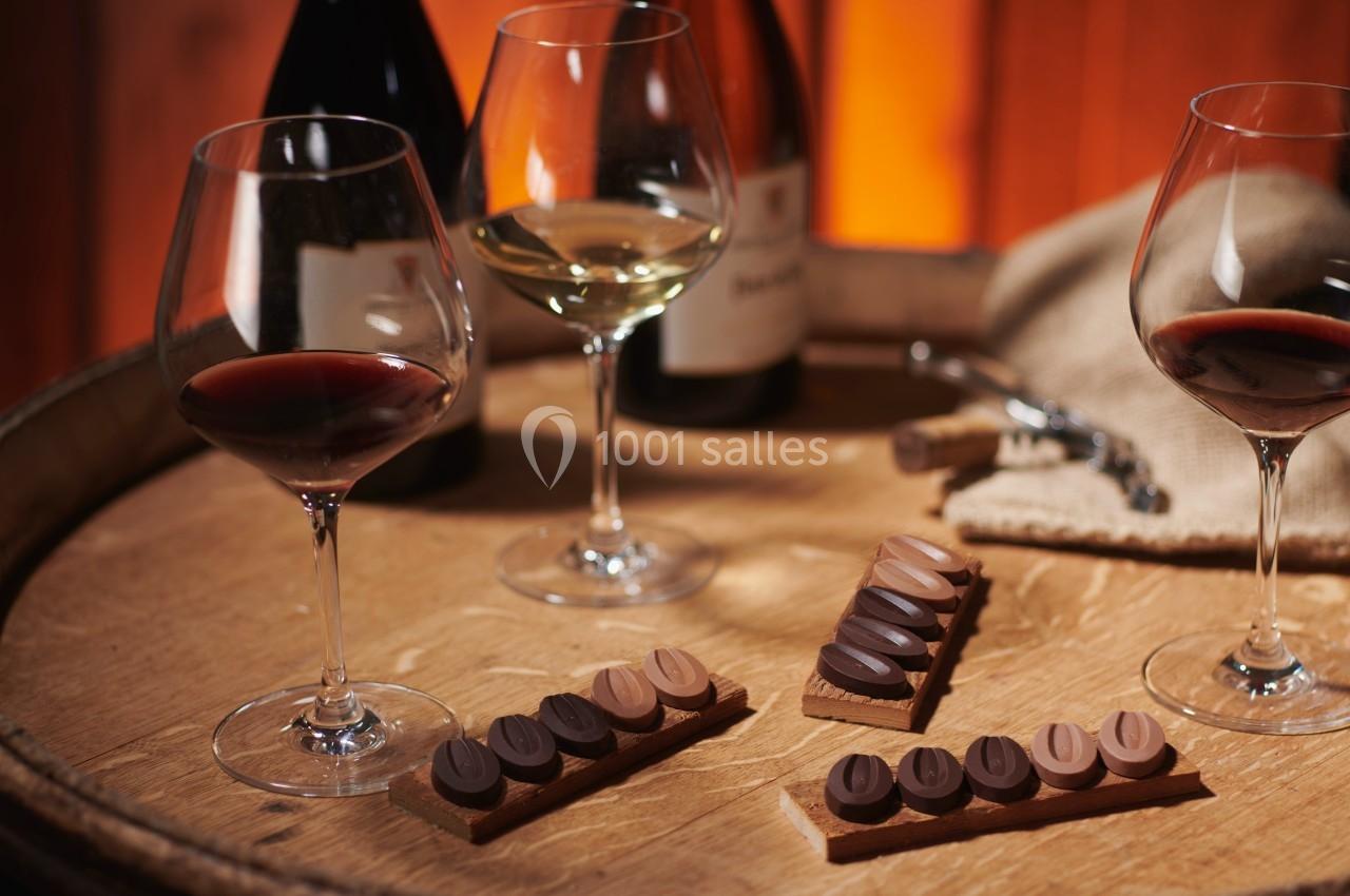 Verres de vin rouge et blanc sur un tonneau en bois, accompagnés de chocolats assortis disposés sur des tablettes.