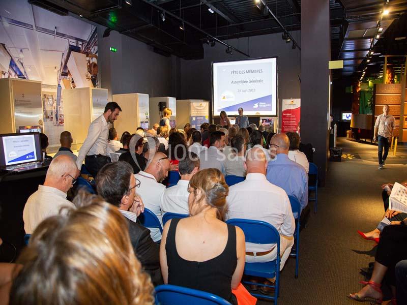 Personnes assises dans une salle de conférence, regardant une présentation projetée sur un écran.