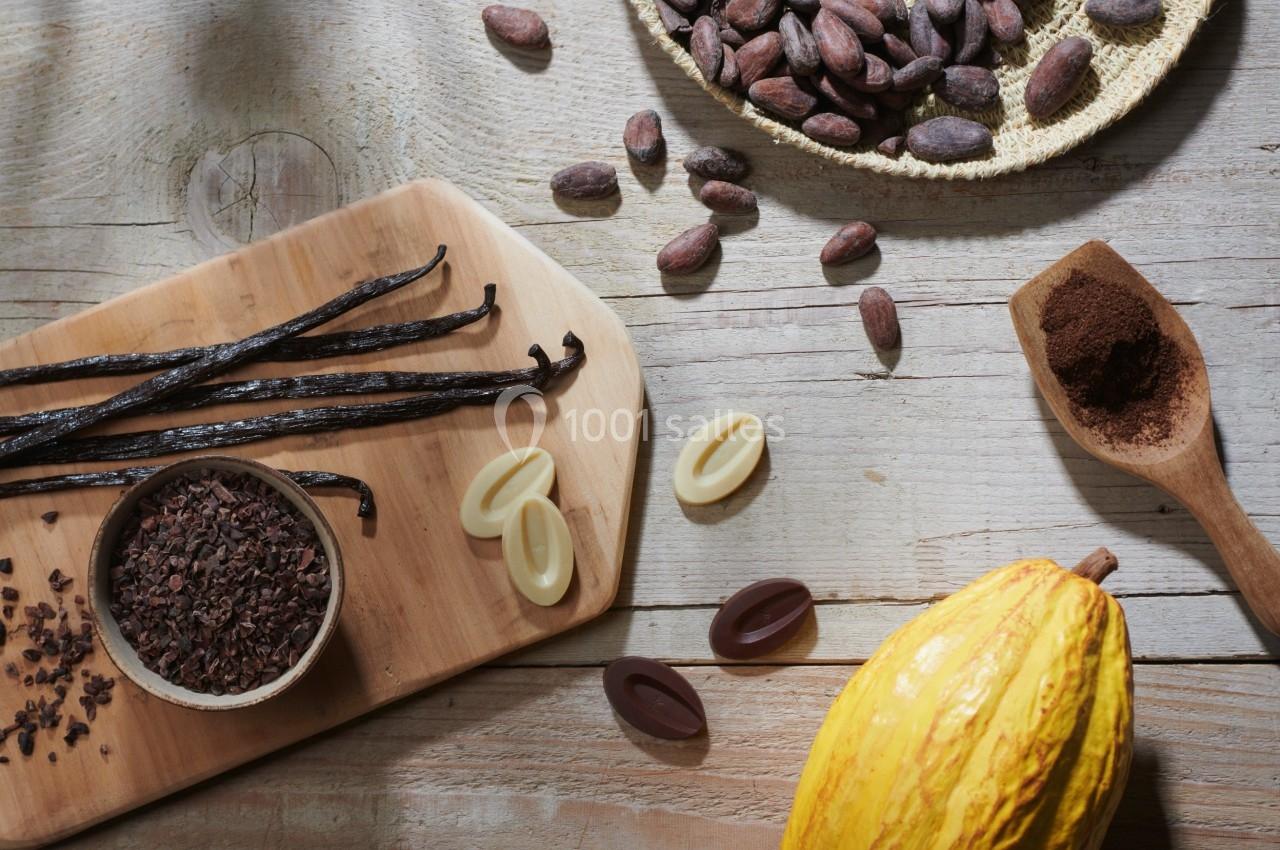 Fèves de cacao, gousses de vanille, poudre de cacao et chocolat disposés sur une table en bois.