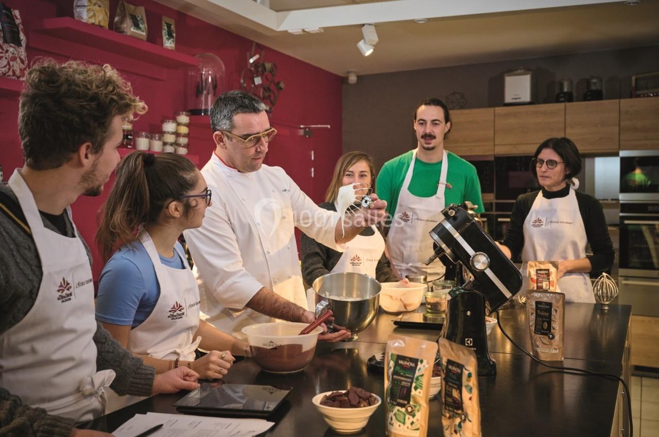 Un chef pâtissier enseigne à un groupe de personnes en tabliers autour d'un plan de travail avec des ingrédients.