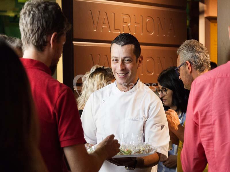 Un chef en tenue blanche sourit en servant des plats à un groupe de personnes lors d'un événement convivial.