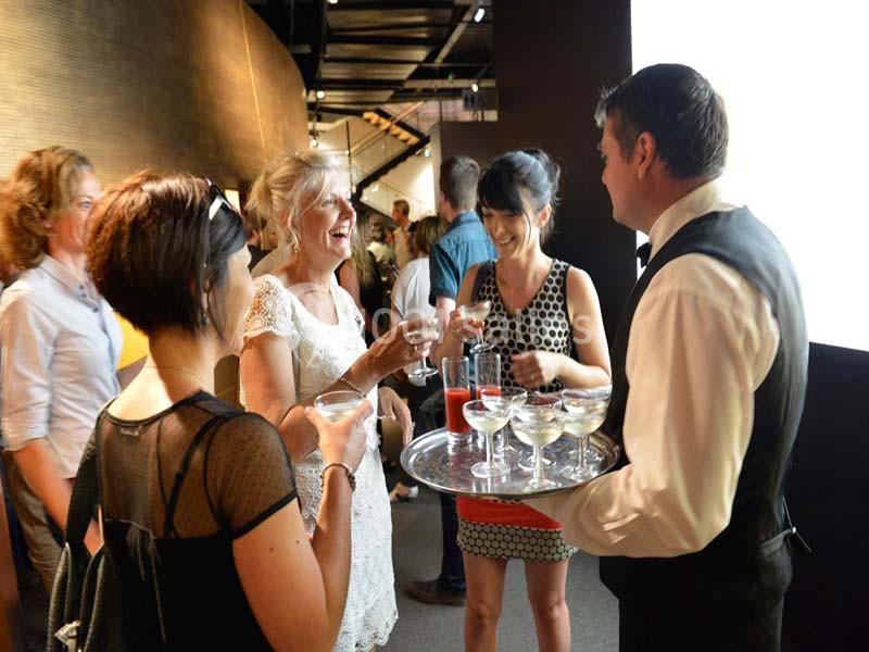 Un serveur propose des verres de champagne à un groupe de personnes discutant dans un cadre élégant.