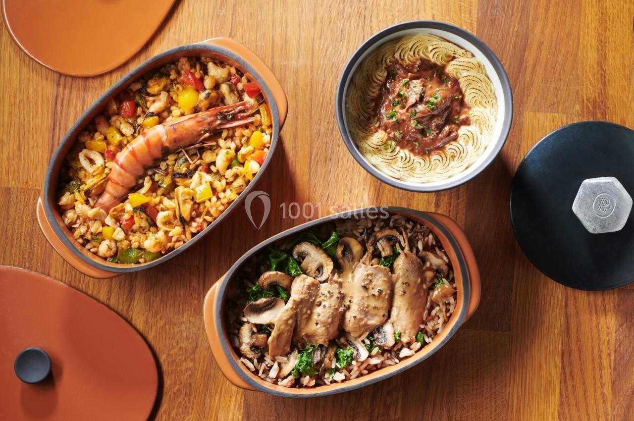 Trois plats cuisinés : paella aux fruits de mer, champignons sautés et purée avec sauce, sur une table en bois.