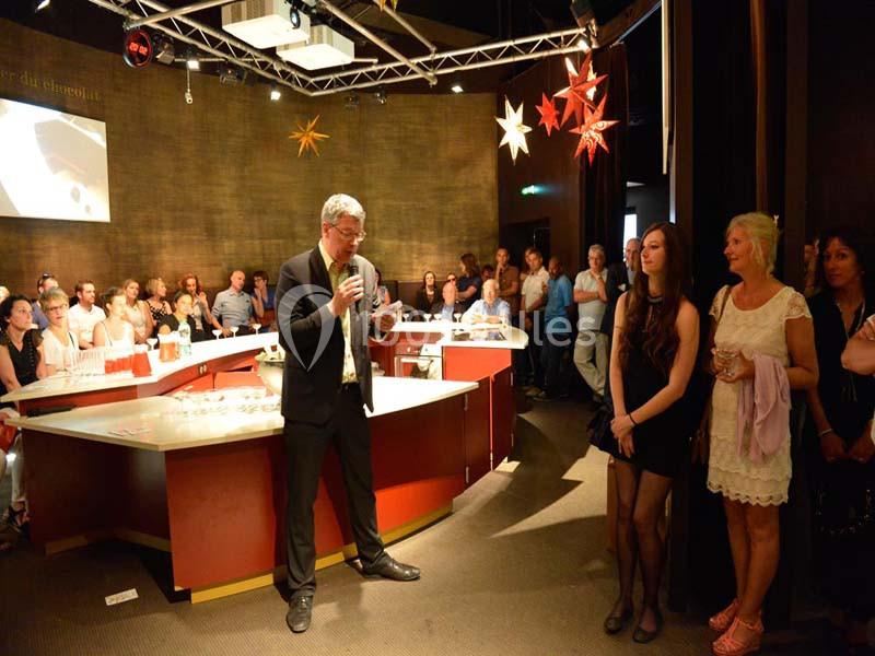 Un homme en costume parle au micro devant un public rassemblé dans une salle décorée d'étoiles suspendues.