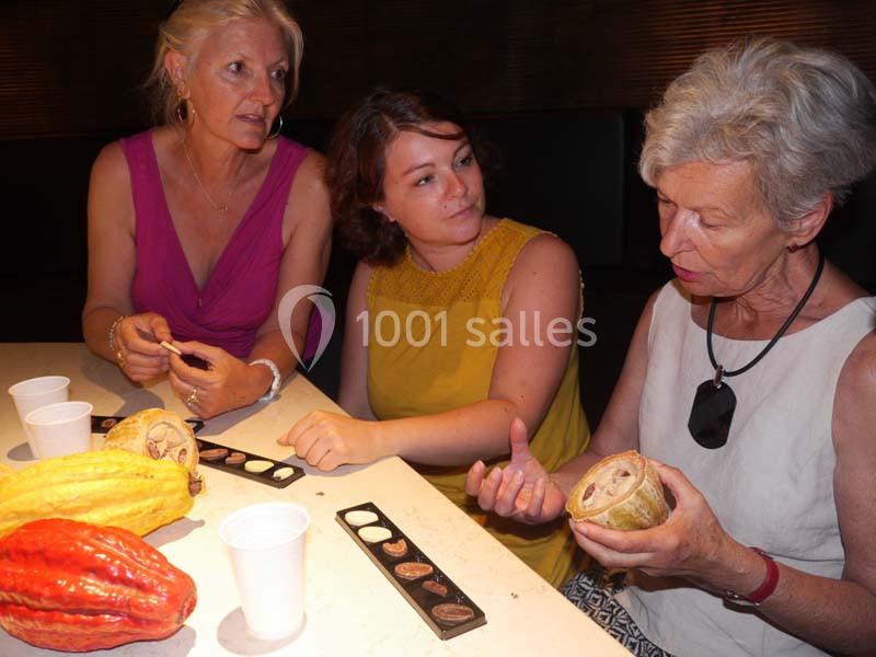 Trois femmes discutent autour de cabosses de cacao et de chocolats disposés sur une table.