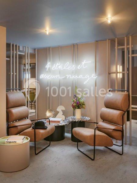 Espace lounge avec fauteuils en cuir beige, table basse, bouquet de fleurs et néon indiquant ’4 étoiles et aucun nuage’.