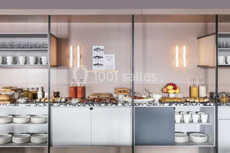 Buffet de petit-déjeuner avec boissons, fruits, viennoiseries, pains et vaisselle disposés sur des étagères et un comptoir.