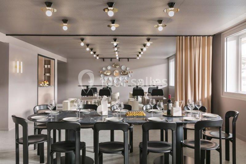 Salle de restaurant moderne avec tables dressées, chaises noires, éclairage design et décoration murale circulaire.