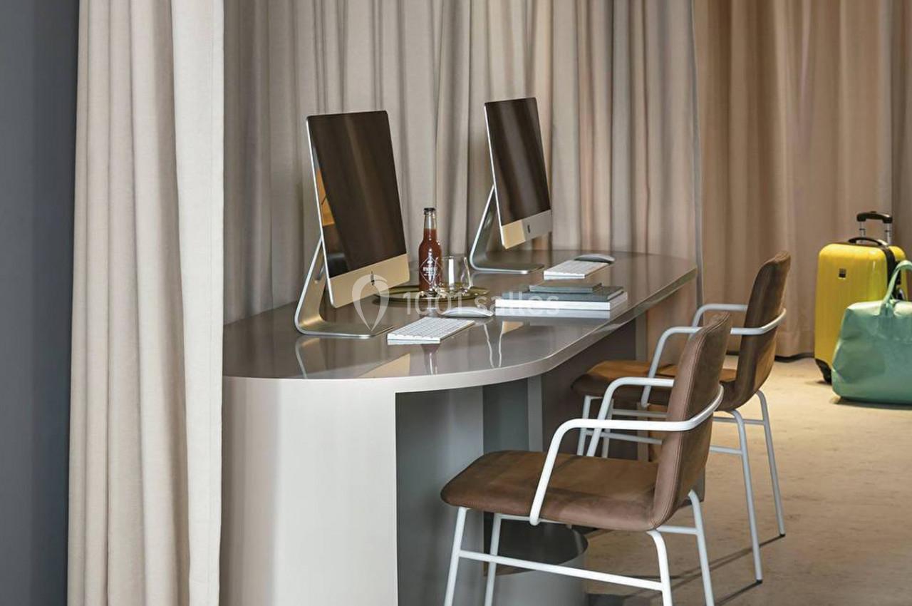 Deux ordinateurs sur un bureau moderne avec chaises, une valise jaune et un sac vert en arrière-plan.