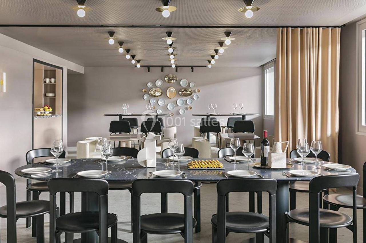 Salle à manger moderne avec grande table noire, chaises assorties, vaisselle dressée et décor mural en assiettes.