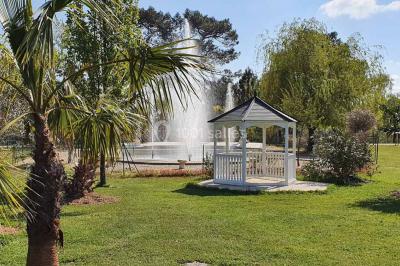 Kiosque décoré de fleurs blanches au bord d'un lac avec une fontaine, sous un ciel dégagé.