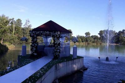 Kiosque décoré de fleurs blanches au bord d'un lac avec une fontaine, sous un ciel dégagé.