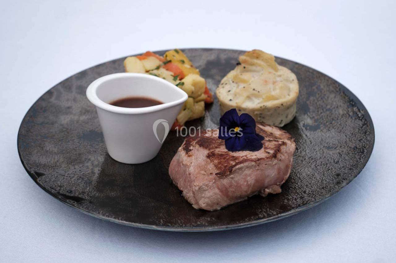 Assiette avec un filet de viande, une sauce en ramequin, des légumes et un gratin, décorée d'une fleur comestible.