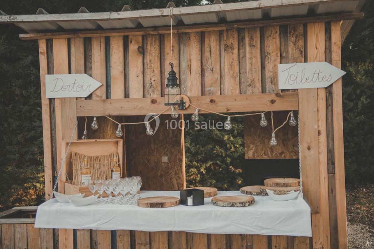 Stand en bois décoré avec des guirlandes lumineuses, proposant des verres et des bouteilles, entouré de panneaux…