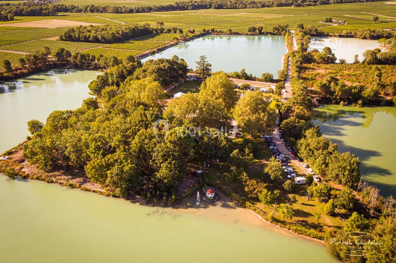 Vue aérienne d'une île boisée entourée de lacs, avec des champs et une route bordée de voitures à proximité.