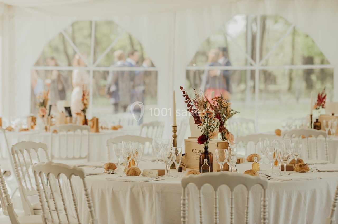 Tables décorées avec des fleurs et de la vaisselle dans une salle lumineuse, avec des invités flous en arrière-plan.