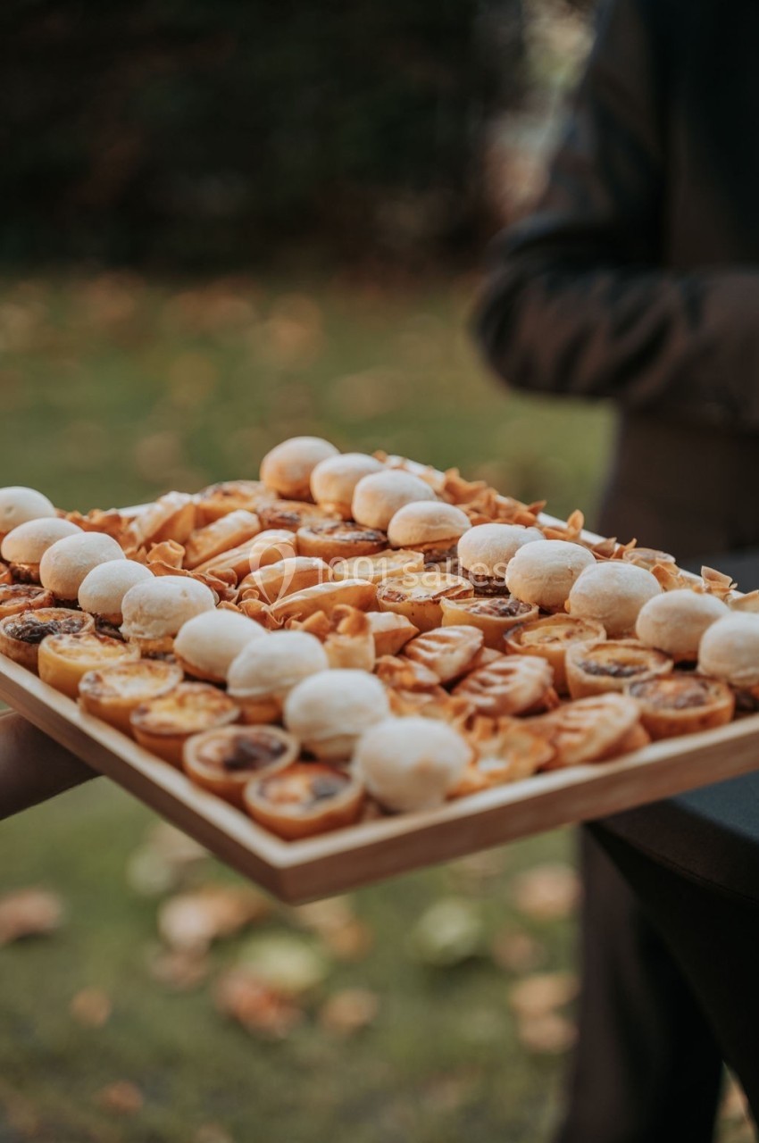 Plateau en bois garni de bouchées salées variées, présenté en extérieur avec un fond flou de verdure.