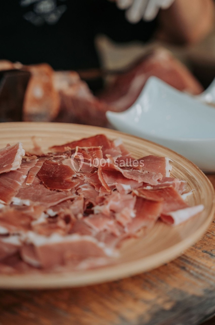 Assiette en bois contenant des tranches fines de jambon cru, posée sur une table en bois.