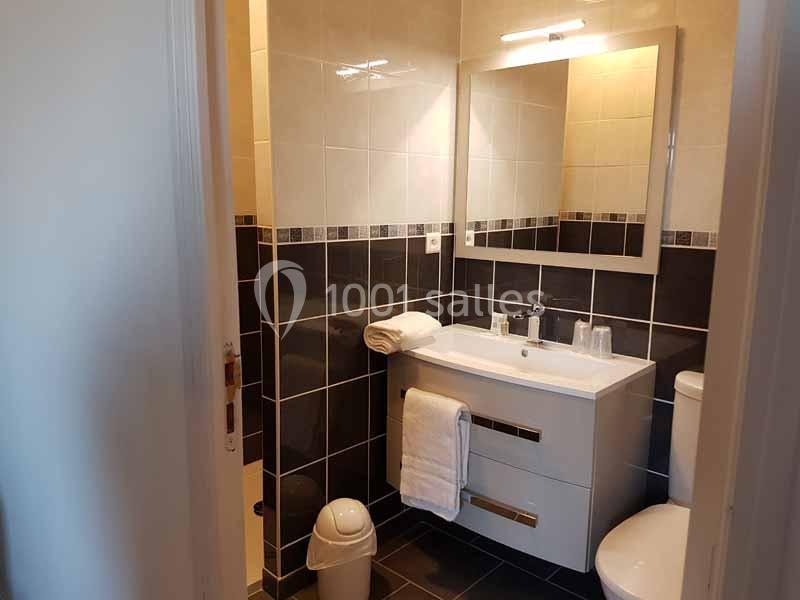 Salle de bain avec lavabo, miroir éclairé, serviettes pliées, poubelle et carrelage noir et blanc.