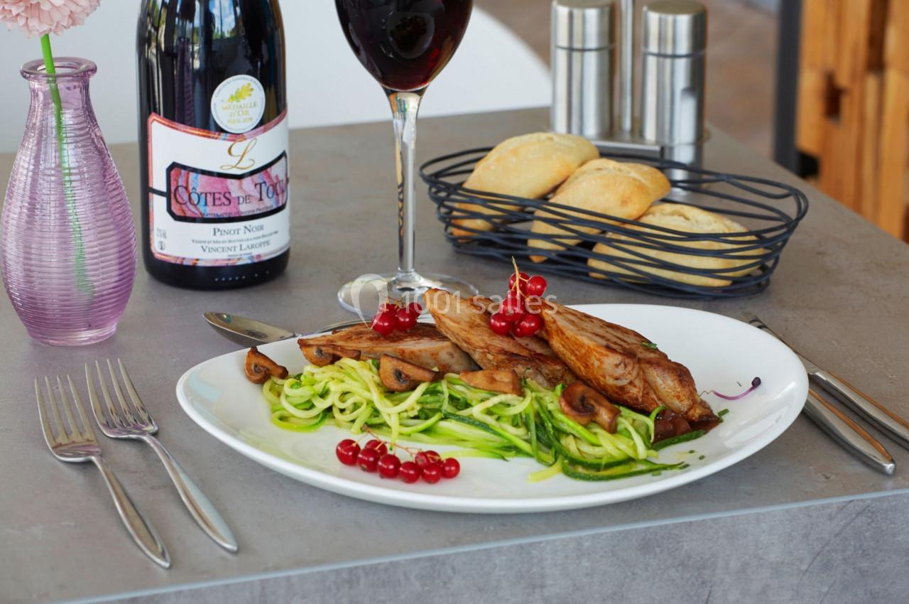Assiette de courgettes en spirales avec viande grillée, champignons, groseilles rouges, pain et verre de vin rouge.