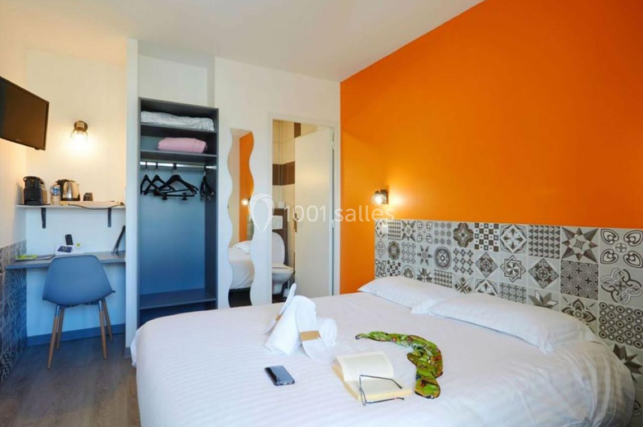 Chambre d'hôtel avec lit double, bureau, télévision murale, armoire ouverte et mur orange vif.